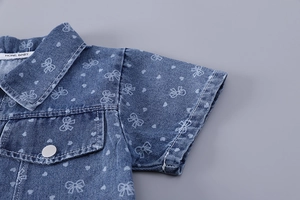 Gros plan d'une chemise en jean fille avec motifs noeuds blancs et poche de poitrine