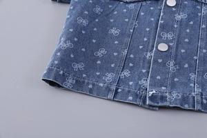 Détail du tissu denim bleu avec imprimés cœurs et nœuds blancs et boutons-pression argentés