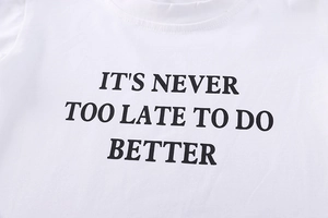 Detail of white cotton sweatshirt featuring black 'IT'S NEVER TOO LATE' slogan print