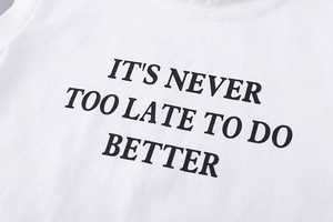 Detail of white cotton T-shirt featuring bold black slogan It is never too late to do better
