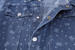 Détail de tissu denim bleu avec imprimés nœuds et cœurs et boutons-pression argentés