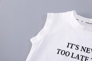 Close-up of cotton baby vest neckline with 'IT'S NEVER TOO LATE' print and ribbon detail