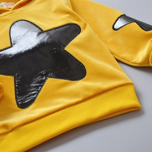 Detail of yellow hooded sweatshirt with metallic star patch and soft fabric texture