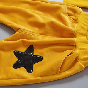 Detailed macro view of yellow velvet kids' joggers featuring sequin star patch and ribbed cuffs