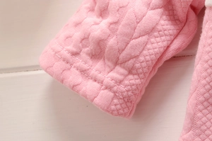 Détail du poignet d'un sweat rose pour bébé avec maille torsadée et motif matelassé