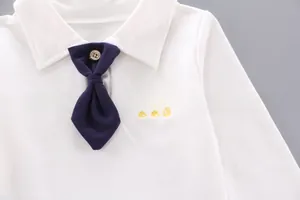 Detail of white long-sleeved polo shirt with embroidered yellow crown and blue bowtie