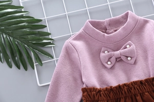 Close-up of pink knit top with bow and pearls paired with coffee pleated skirt