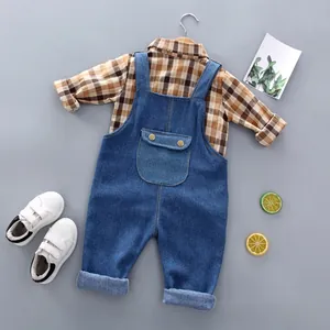 Flat lay of brown plaid shirt and denim overalls set for children with white sneakers