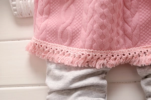 Détail macro du pull en maille rose à franges et leggings gris sur fond de bois