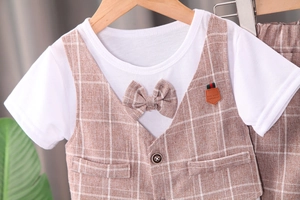 Détail d'un ensemble pour bébé avec gilet à carreaux marron et nœud papillon blanc