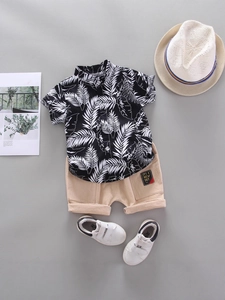 Boys summer outfit with palm leaf print shirt and khaki shorts on a grey background