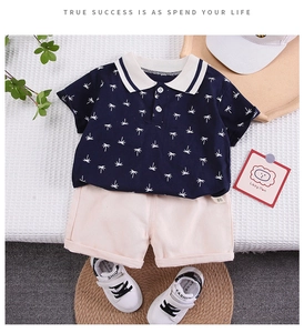 Flat lay of boys summer outfit featuring navy coconut print polo shirt and beige shorts
