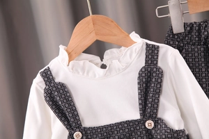 Détail du col à volants sur chemise blanche et bretelles à carreaux gris avec boutons