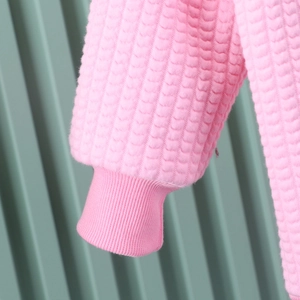 Detail of pink girl's jacket cuff featuring textured heart-shaped quilted fabric patterns