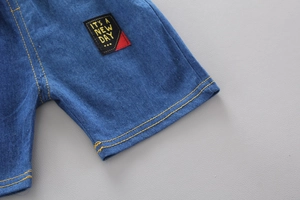 Detail of blue denim shorts showing yellow stitching and black IT'S A NEW DAY patch