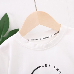 Gros plan sur le col d'un t-shirt blanc pour bébé avec logo HONE BABY et décor de feuilles