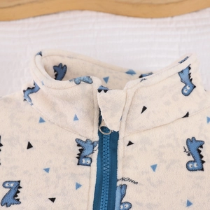 Close-up of children's warm fleece jacket featuring blue dinosaur prints and secure zipper