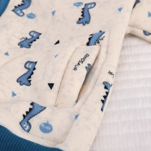Detail of soft fleece fabric featuring blue cartoon dinosaur prints and ribbed hem