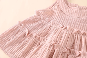 Detail of pink girls' top featuring vertical pleated fabric and layered ruffle collar