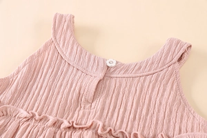 Detail of pink cotton ruffle top featuring a white flower button and ribbed texture