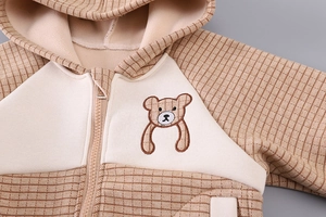 Detailed view of kids winter jacket with cute bear embroidery and beige plaid fabric textures