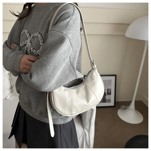 Model wearing a cream crescent underarm bag with vertical stitching and leather strap