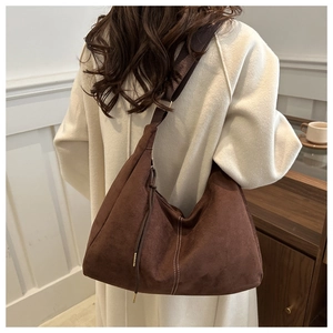 Dettaglio di una borsa hobo in pelle scamosciata marrone con coulisse e tracolla larga