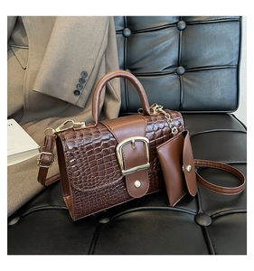 Close-up of brown croc-effect handbag with gold buckle and mini pouch on leather sofa