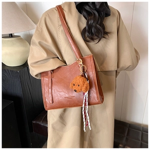 Dettaglio borsa tote in pelle marrone con scritta 'Fashion', ciondolo teddy e nastro