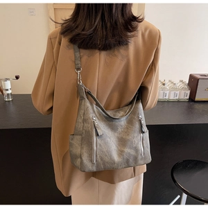 Detail of grey hobo bag with silver zippers shown on a model in a cafe setting