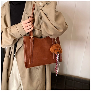 Dettaglio della borsa tote vintage marrone con ciondolo a cane e sciarpa a righe decorativa
