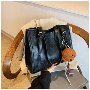 Dettaglio di borsa tote in pelle nera con ciondolo a forma di cane su sedia in legno