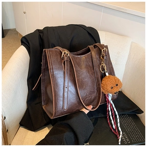 Dettaglio della grande borsa tote marrone scuro con trama in pelle oliata e orsetto