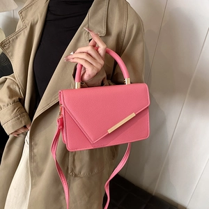 Vibrant pink leather crossbody square bag with gold hardware held by a model in a trench coat
