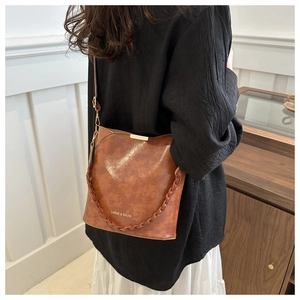 Retro caramel leather bucket bag with woven handle and adjustable strap worn by model