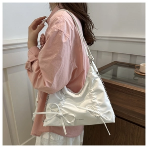 Detail of white pleated tote bag with bow accent and silver chain strap on model