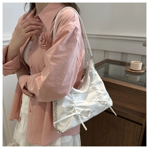 Detail of white pleated tote bag with bow accents and silver chain strap on shoulder