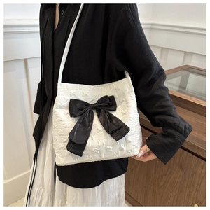 Close-up of white bucket bag featuring star texture and a large black bow detail