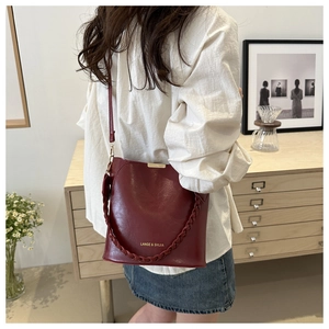 Detail of burgundy leather bucket bag featuring woven handle and gold brand lettering