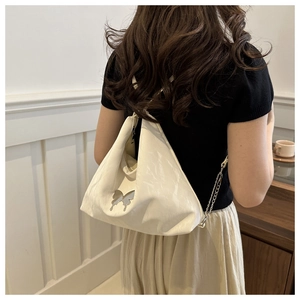 Détail du sac crème avec papillon métallique et bandoulière chaîne porté par un mannequin