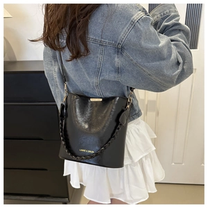 Detail of a black leather bucket bag with woven handle and gold hardware in daily use