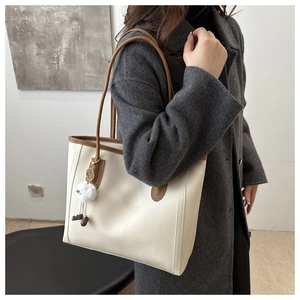 Cream tote bag with brown leather trim and plush charm shown on a model's shoulder