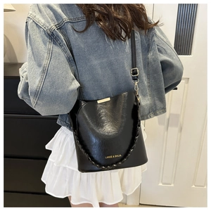 Detail of black glossy bucket bag with gold metal trim and woven handle
