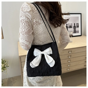 Black tote bag with large white bow detail shown on a model in a cozy home setting