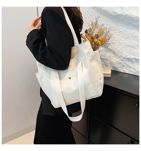 Detail of white canvas tote bag showing wide straps, outer pocket and button closure