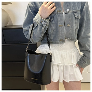Detail of minimalist black leather bucket bag with gold hardware and woven strap