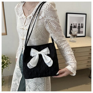 Detail of black bubble fabric tote bag featuring a large white organza bow and slim straps
