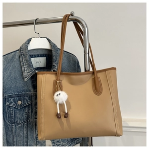 Detail of camel tote bag with brown contrast trim and a white plush charm accessory