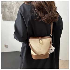 Detail of a two-tone bucket bag with suede texture and a plush charm on a black coat