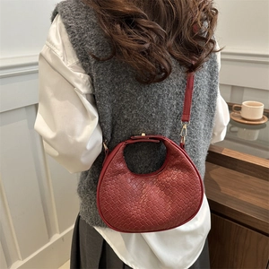 Deep red woven crescent handbag with crossbody strap shown on a model in a cozy setting
